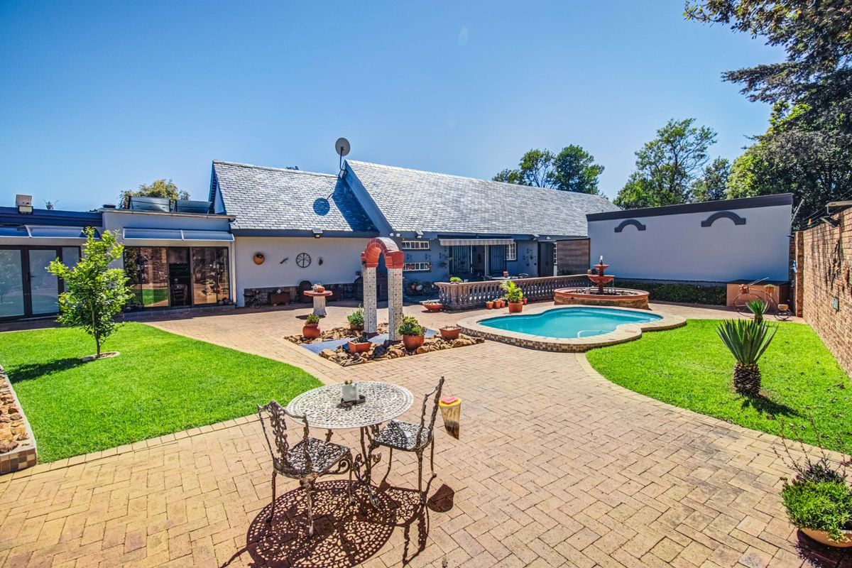 Spacious rear garden featuring a paved patio, swimming pool, decorative water feature, and well-maintained lawn, providing an ideal outdoor entertainment area.