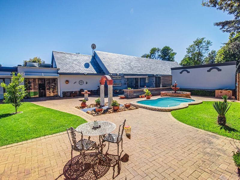 Spacious rear garden featuring a paved patio, swimming pool, decorative water feature, and well-maintained lawn, providing an ideal outdoor entertainment area.