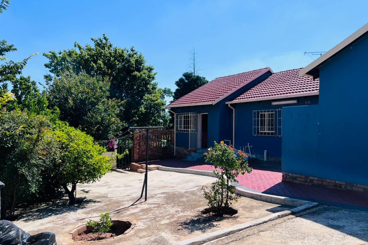 Rear view of the house featuring a paved patio area, security bars on windows, and a tiled roof, set within a garden space.