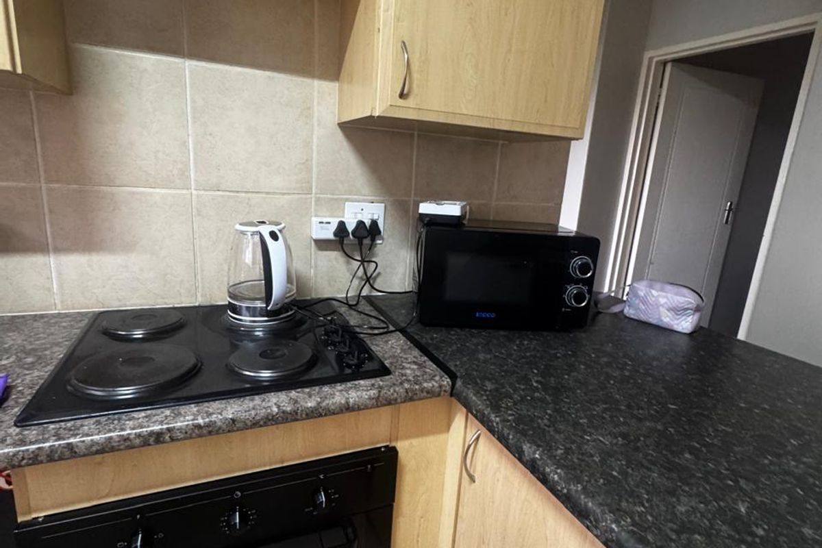 A functional kitchen featuring light wood-tone cabinetry, dark laminate countertops, a built-in oven, and an electric hob with tiled splashback.