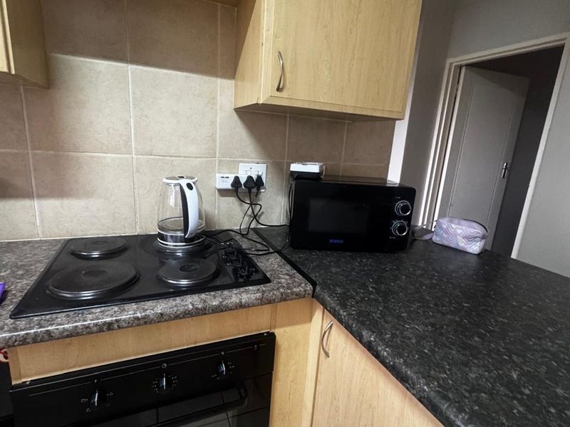 A functional kitchen featuring light wood-tone cabinetry, dark laminate countertops, a built-in oven, and an electric hob with tiled splashback.