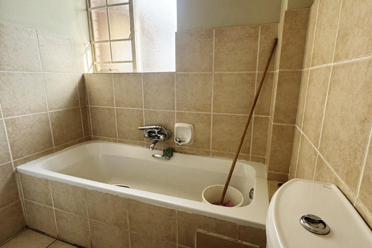 A functional bathroom featuring a bathtub with tiled surround, a standard toilet, and tiled flooring, offering a practical layout for daily use.