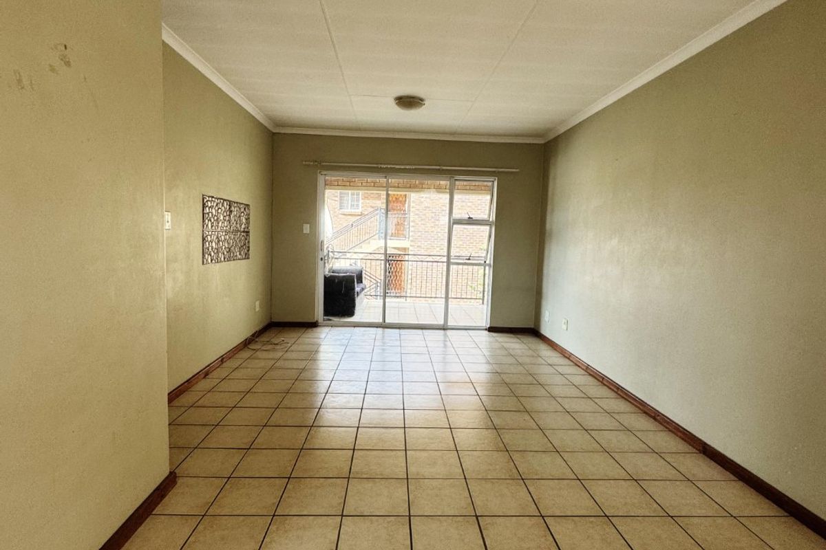 An empty, open-plan living area featuring neutral tiled flooring, sliding glass doors leading to a balcony, and simple cornice detailing.