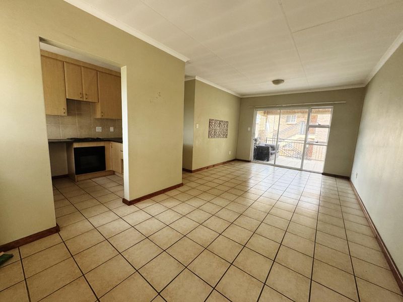 Open plan living area featuring tiled flooring and a compact kitchen with built-in cabinetry, oven, and hob, leading to a sliding door balcony access.