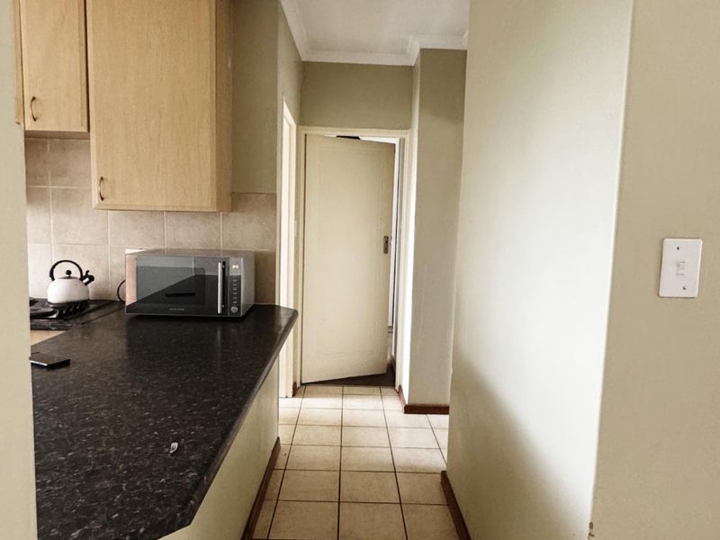 A functional kitchen area featuring laminate cabinetry, dark granite countertops, and tiled flooring, leading into a hallway with a standard interior door.