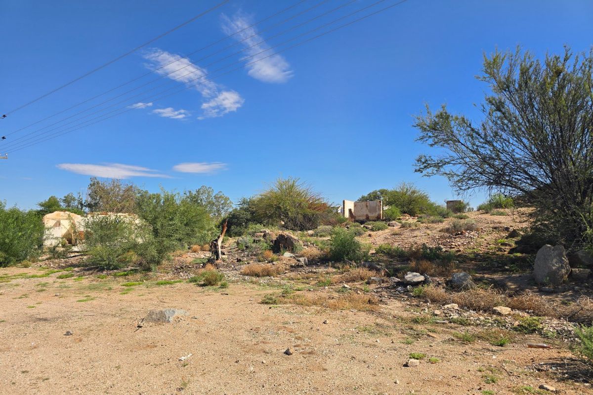 A view of a vacant commercial plot featuring remnants of dilapidated masonry structures and natural, undeveloped terrain.