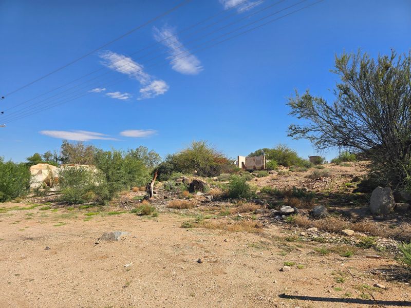 A view of a vacant commercial plot featuring remnants of dilapidated masonry structures and natural, undeveloped terrain.