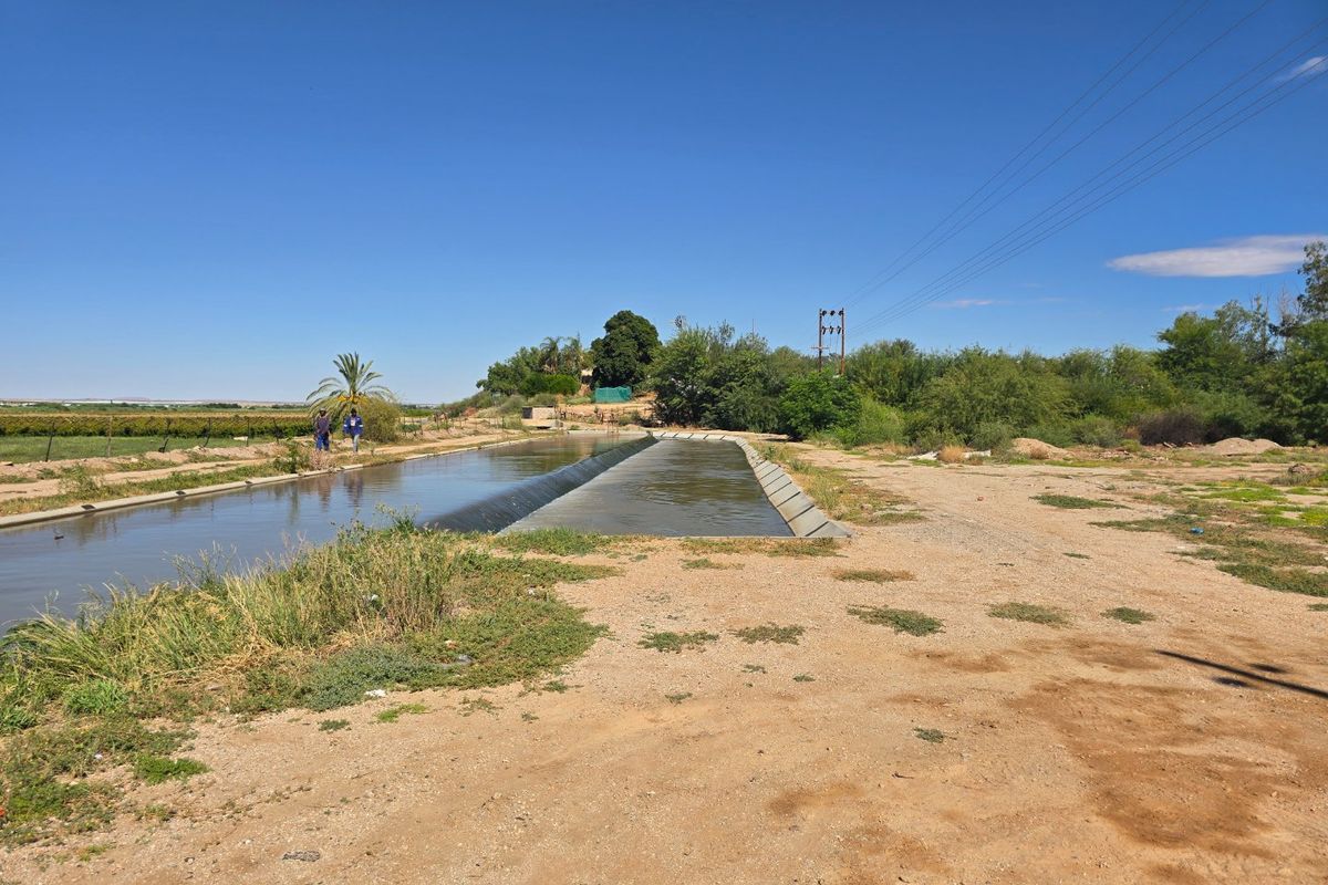An outdoor view of a concrete irrigation canal running through a rural landscape with overhead power lines visible in the background.
