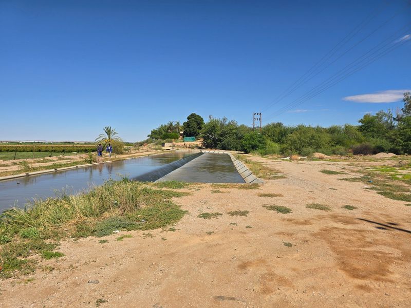 An outdoor view of a concrete irrigation canal running through a rural landscape with overhead power lines visible in the background.