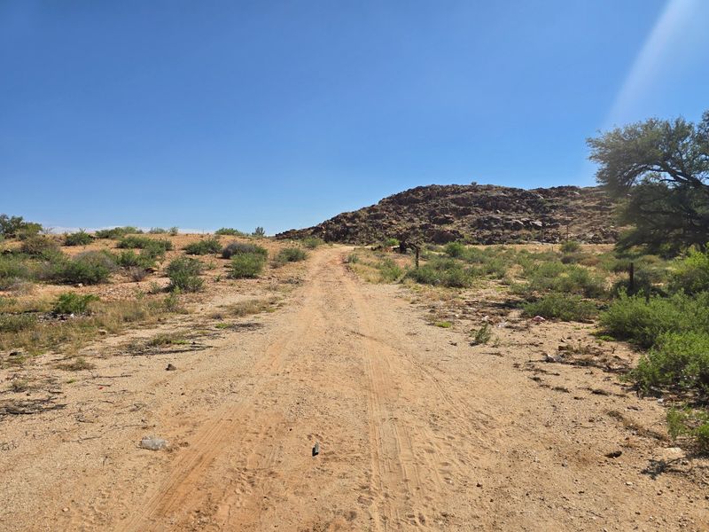 An unpaved dirt access road leading through a rocky, undeveloped landscape with natural vegetation.