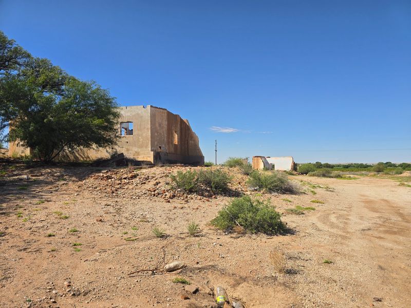 A view of a derelict property featuring ruined masonry structures on a large, undeveloped plot of land.