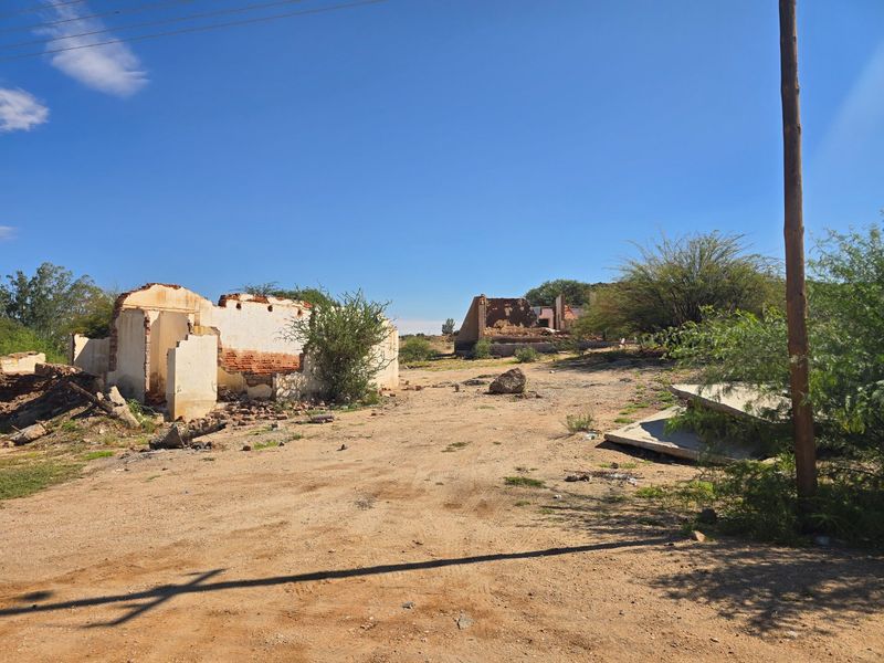 A vacant commercial plot featuring the remains of collapsed masonry structures and scattered concrete debris on an open, undeveloped site.
