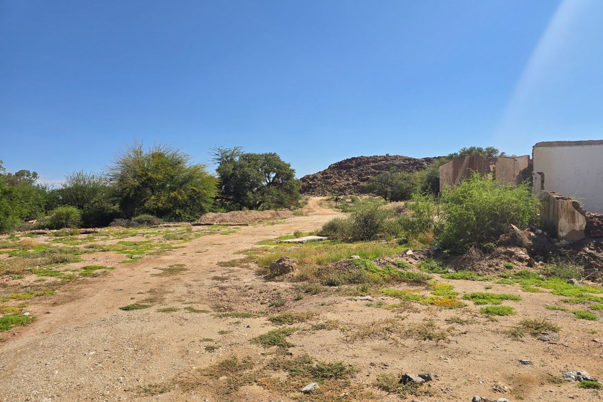 An expansive undeveloped commercial plot featuring natural terrain, sparse vegetation, and the remains of a dilapidated masonry structure.
