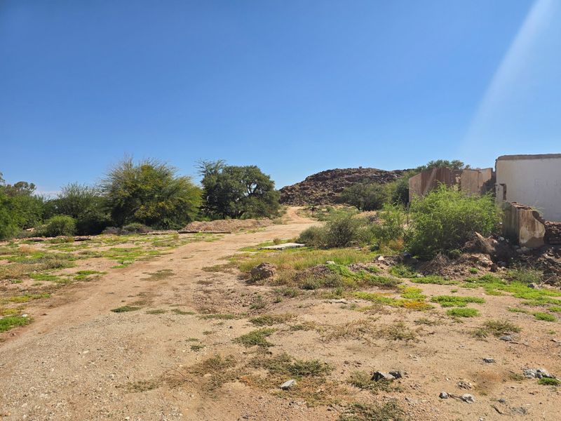 An expansive undeveloped commercial plot featuring natural terrain, sparse vegetation, and the remains of a dilapidated masonry structure.