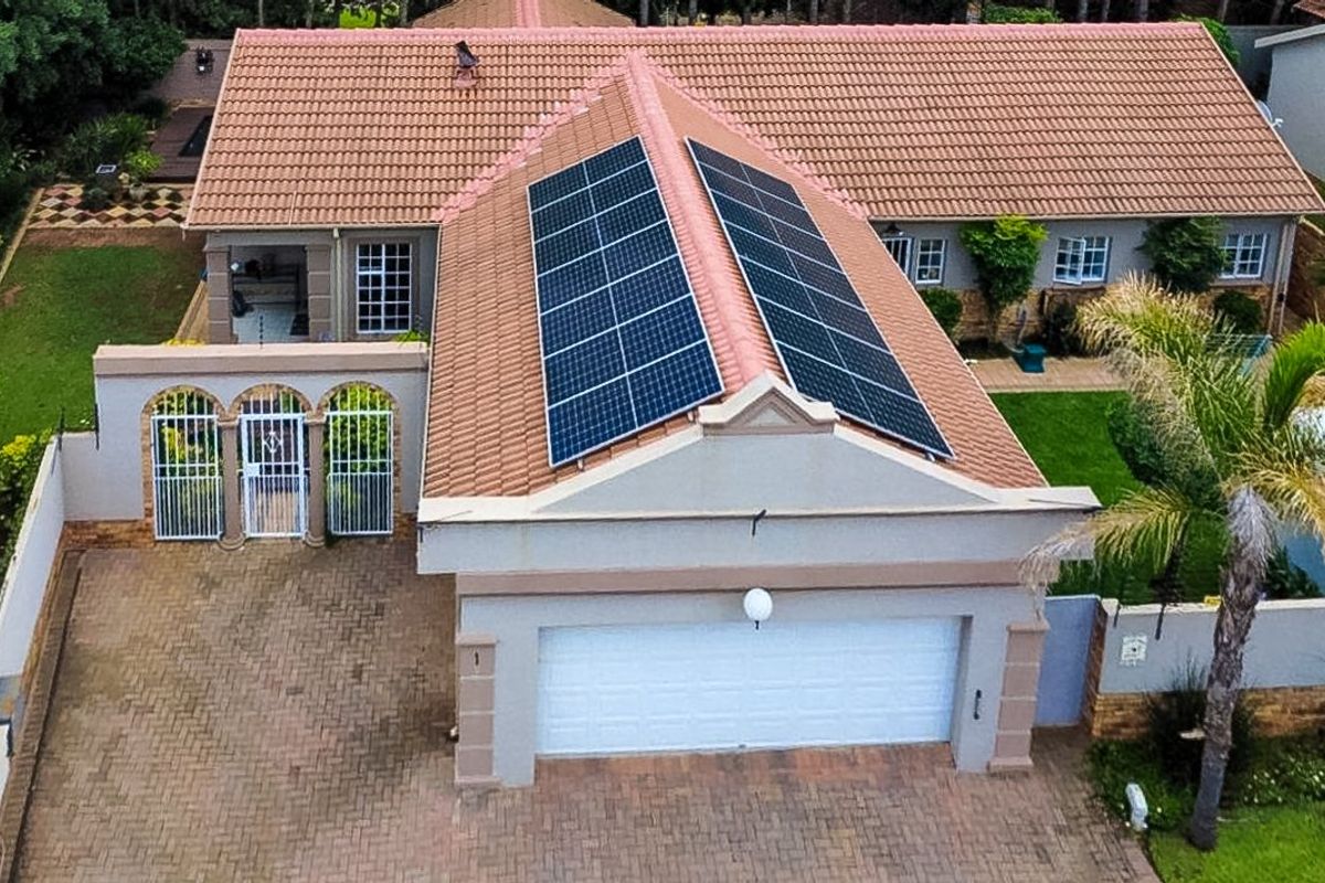 Aerial view of a townhouse featuring a tiled roof with installed solar panels, a paved driveway, and a secure double garage entrance.