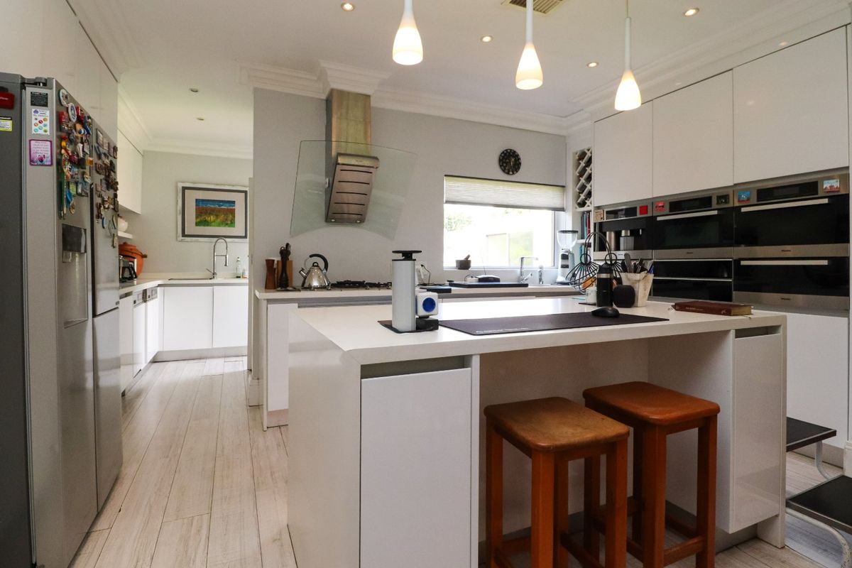 Modern kitchen featuring a central island, high-gloss cabinetry, integrated appliances, and recessed lighting, with an adjacent scullery area.