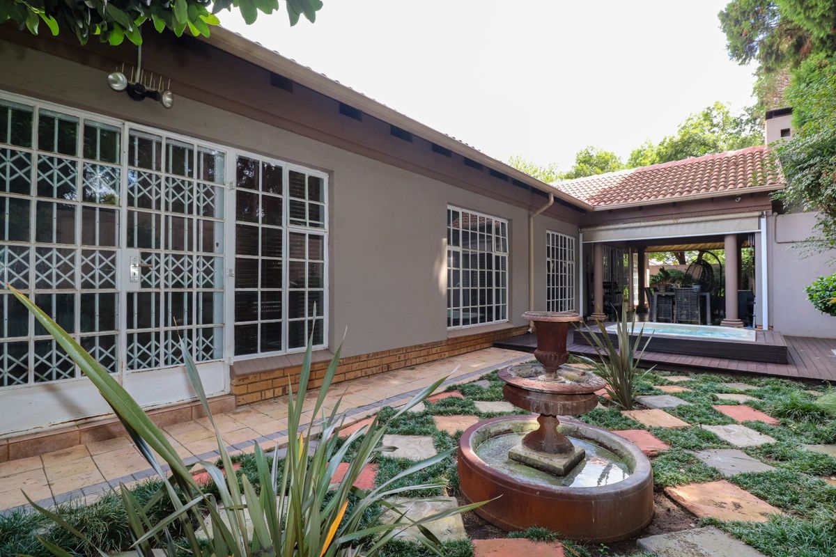 Rear exterior view featuring a landscaped garden with a central water fountain, tiled patio, and a covered deck area with a plunge pool.