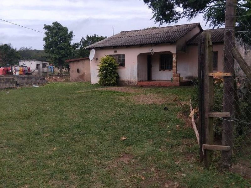 A detached single-story house featuring a covered front porch, tiled roof, and a large surrounding yard enclosed by a wire mesh fence.