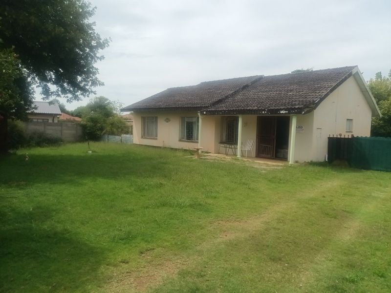 Rear view of a single-story house featuring a covered patio, tiled roof, and a large, expansive garden area.