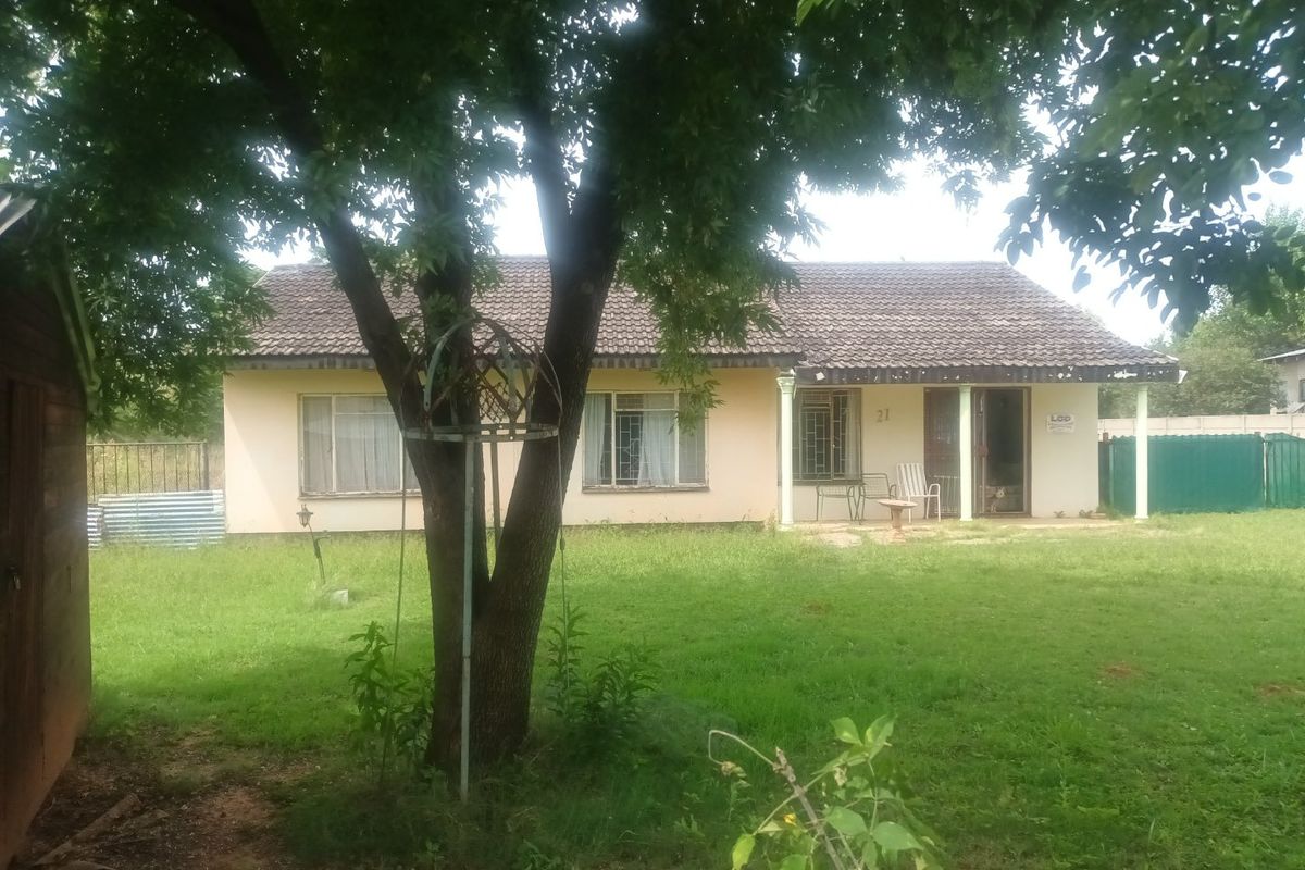 A rear view of a single-story house featuring a tiled roof, a covered patio area, and a spacious garden.