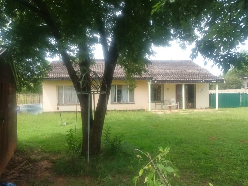 A rear view of a single-story house featuring a tiled roof, a covered patio area, and a spacious garden.