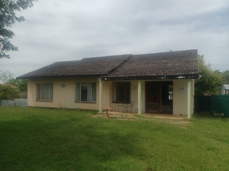 Front elevation of a single-story house featuring a tiled roof, concrete columns, and security gates, set on a large grassed plot.