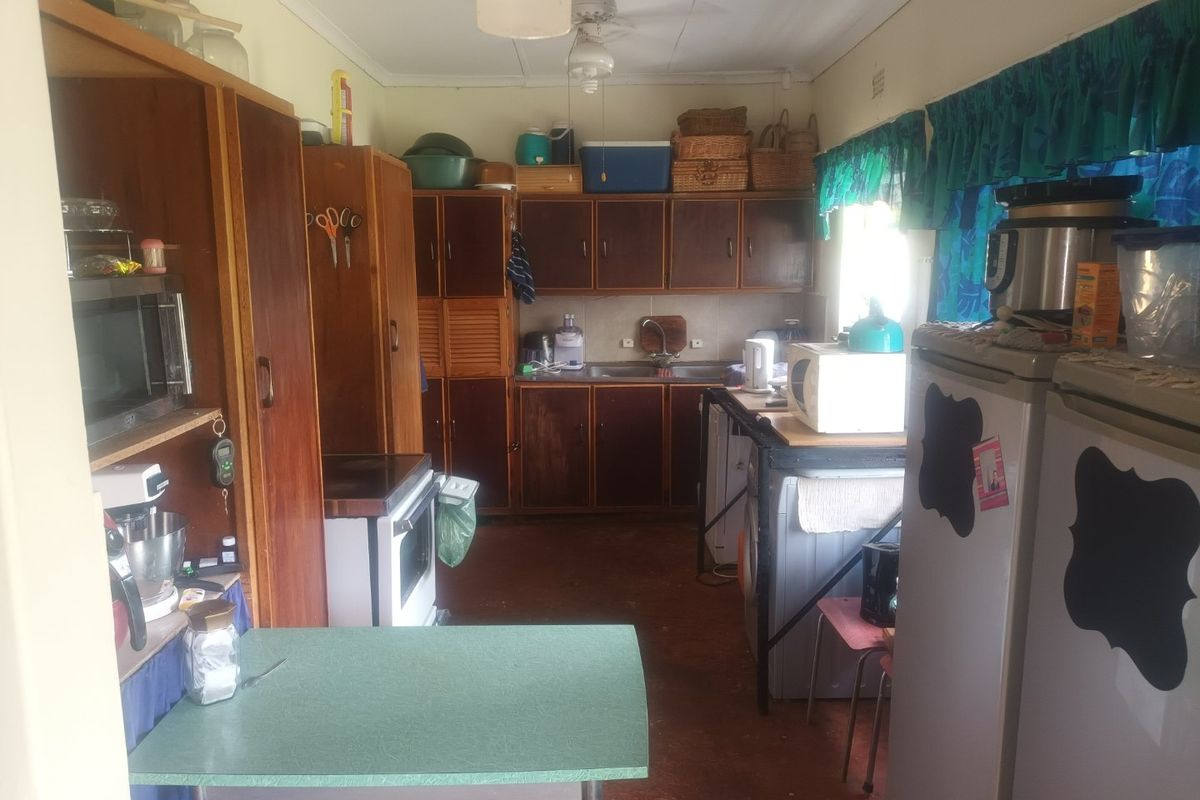 A dated kitchen featuring original wooden cabinetry, a stainless steel sink, and a freestanding oven, offering significant potential for a modern renovation.
