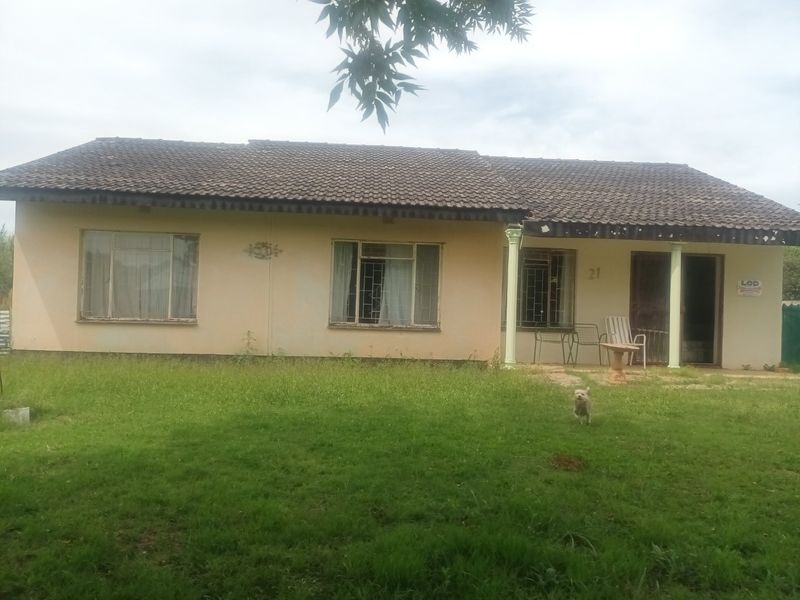 Front elevation of a single-story house featuring a tiled roof, covered porch area, and security bars on windows, set on a large grassed lot.