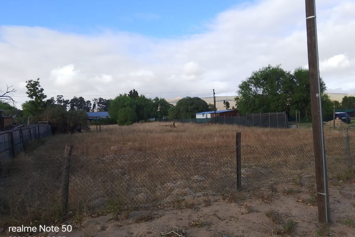 A view of a vacant residential plot featuring wire mesh fencing and a utility pole, set against a natural landscape background.