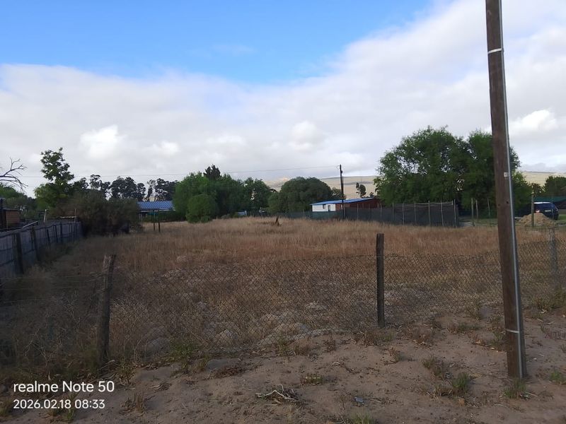 A view of a vacant residential plot featuring wire mesh fencing and a utility pole, set against a natural landscape background.