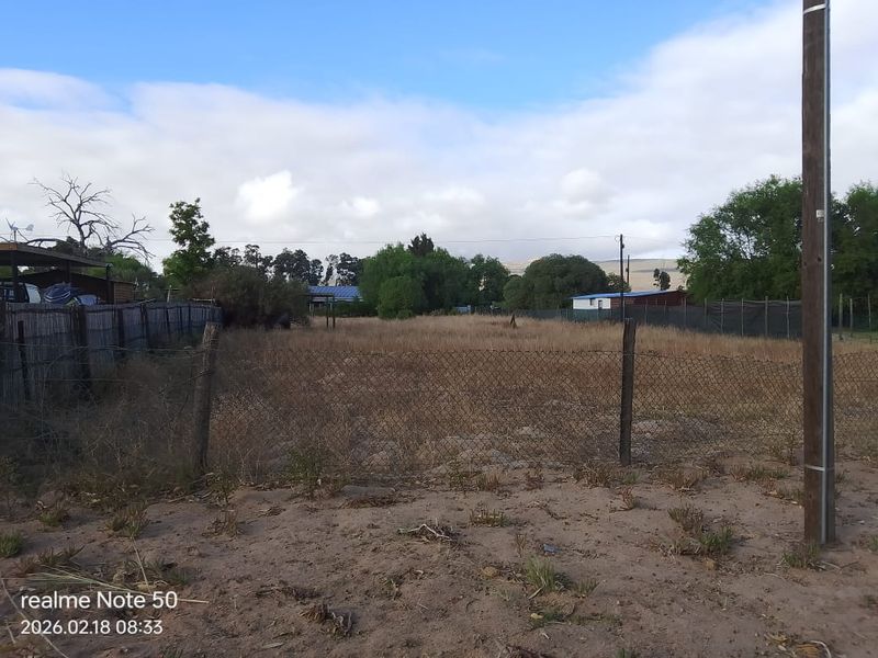 A view of a vacant residential plot featuring chain-link perimeter fencing and a utility pole on a clear day.