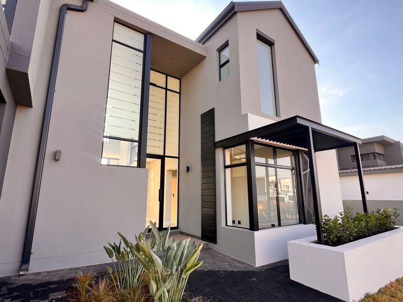 Modern double-storey residence featuring a striking architectural facade with double-volume windows, black aluminium frames, and a neat paved entrance area.
