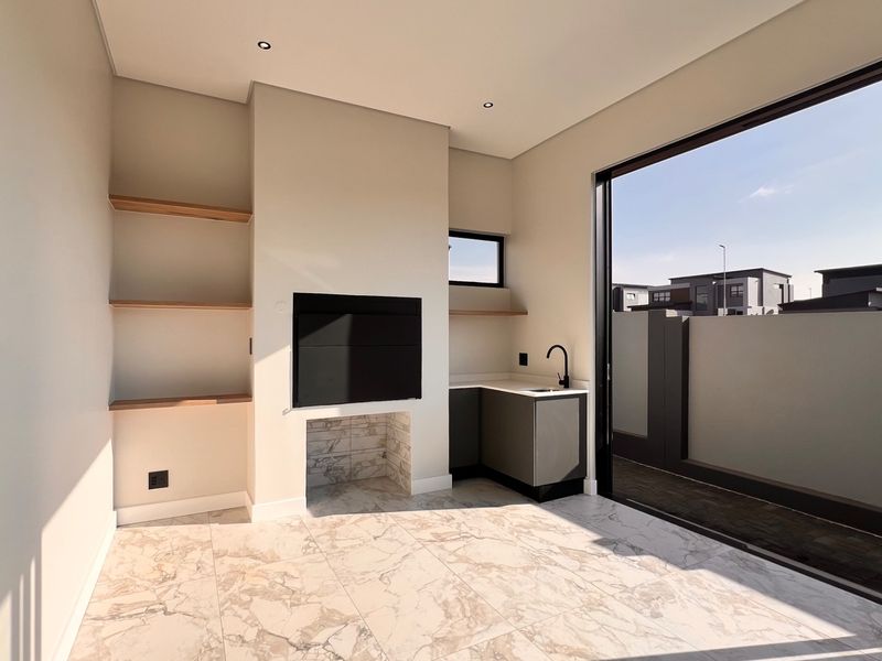 Modern covered patio featuring a built-in braai, kitchenette with sink, marble-look tiling, and large sliding doors opening to the outdoor area.