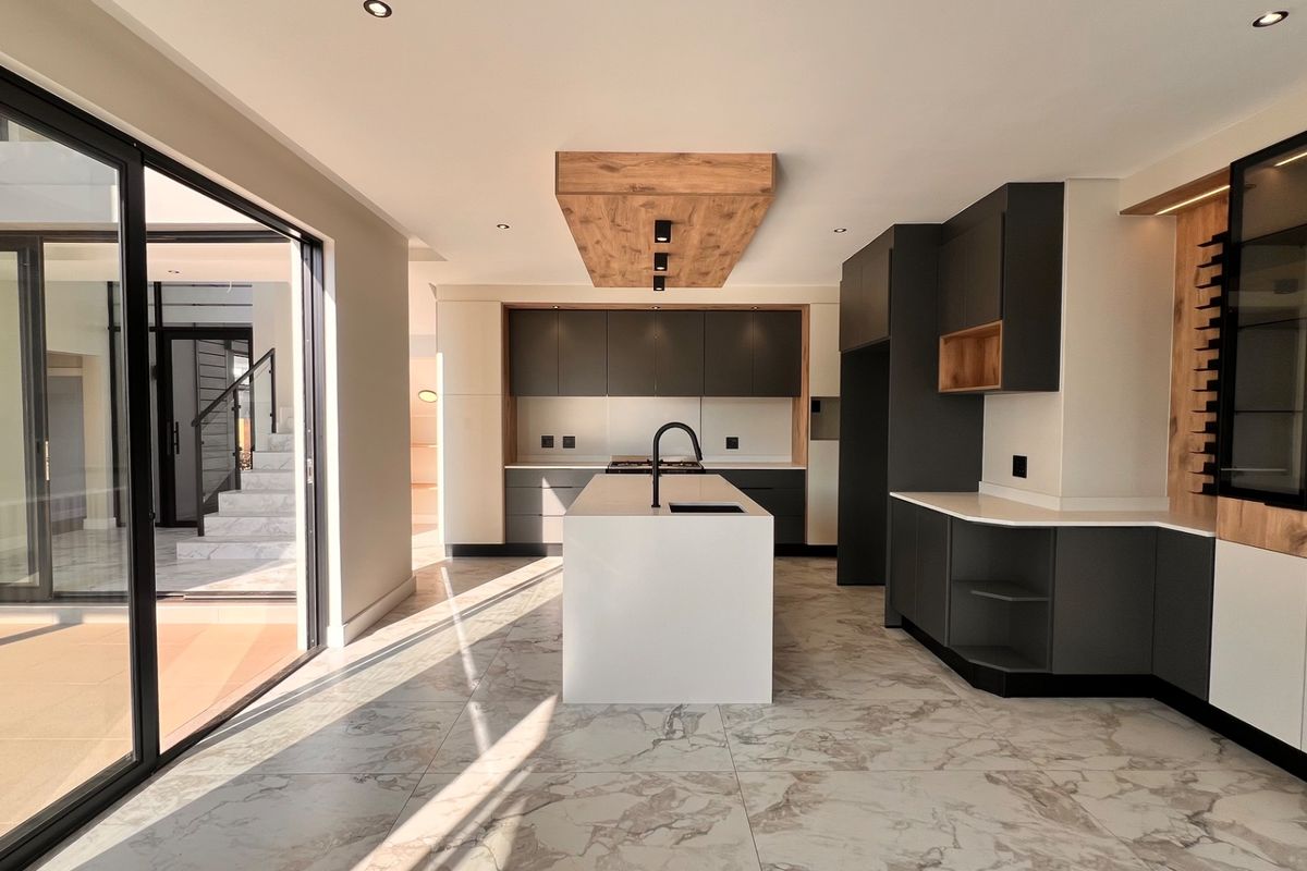 Modern, high-end kitchen featuring a central island, sleek dark cabinetry, stone countertops, and large sliding doors opening to an outdoor area.