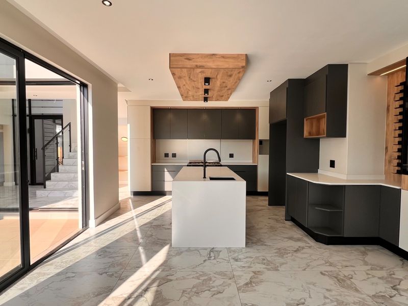 Modern, high-end kitchen featuring a central island, sleek dark cabinetry, stone countertops, and large sliding doors opening to an outdoor area.