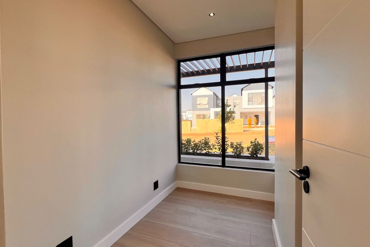 A bright, empty bedroom featuring modern laminate flooring, a large window with exterior views, and clean, neutral finishes.