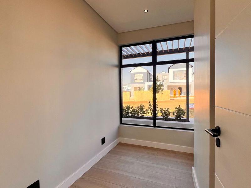 A bright, empty bedroom featuring modern laminate flooring, a large window with exterior views, and clean, neutral finishes.