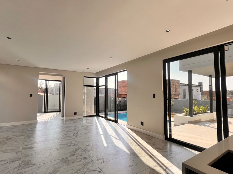 Spacious open-plan living area featuring large format marble-look floor tiles and expansive black aluminium sliding doors providing seamless access to the outdoor pool area.