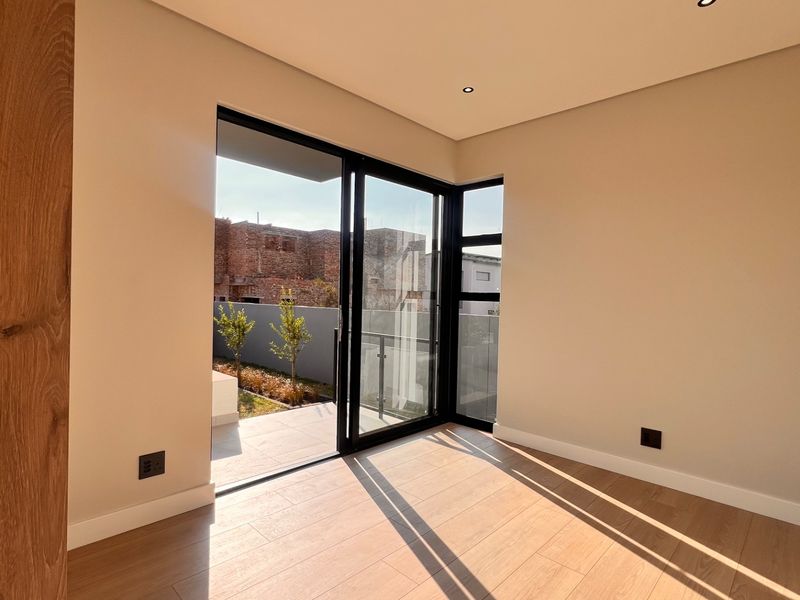 A bright, modern bedroom featuring wood-look tile flooring, recessed lighting, and large sliding glass doors providing access to an outdoor patio area.