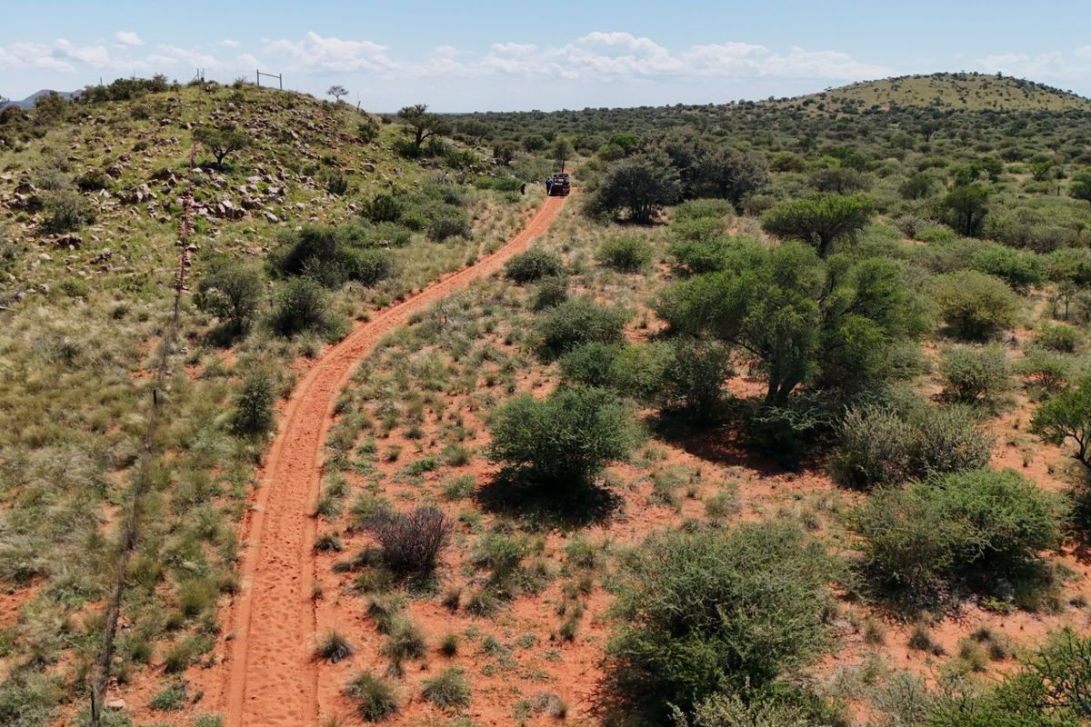 Aerial view of a vast farm landscape featuring a dirt access track, natural bushveld vegetation, and perimeter wire fencing.