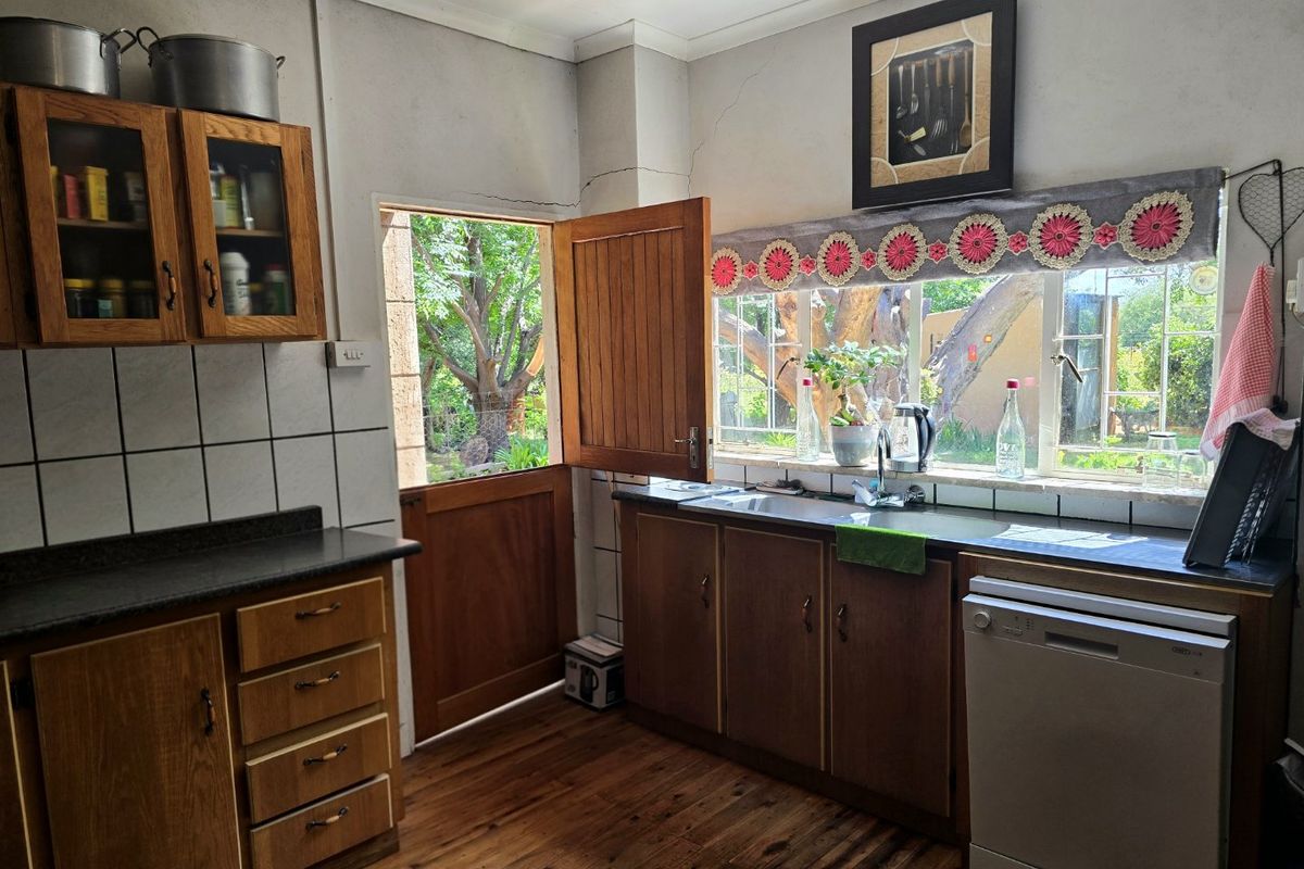 A rustic kitchen featuring wooden cabinetry, laminate countertops, and a stable door leading to the garden, with visible wall cracks requiring maintenance.