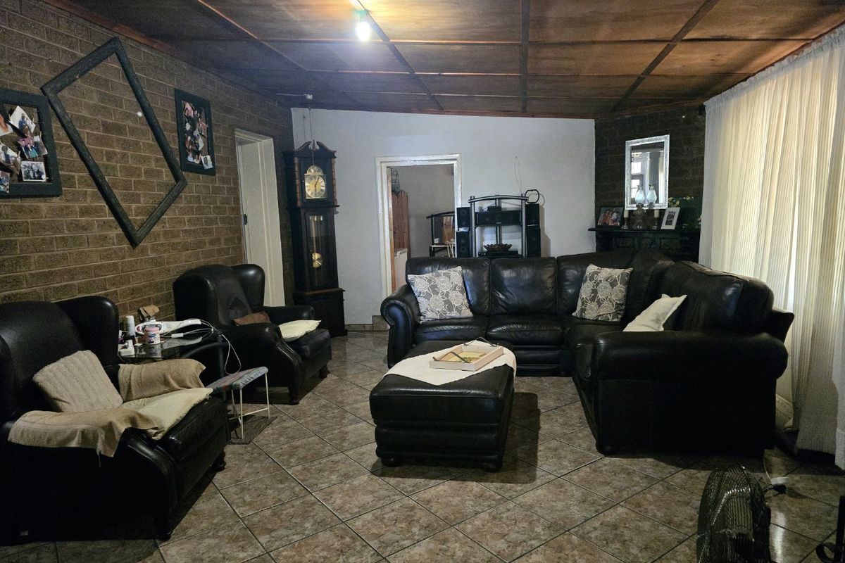 Spacious living room featuring exposed brick walls, tiled flooring, and a timber panel ceiling, creating a warm and rustic atmosphere.