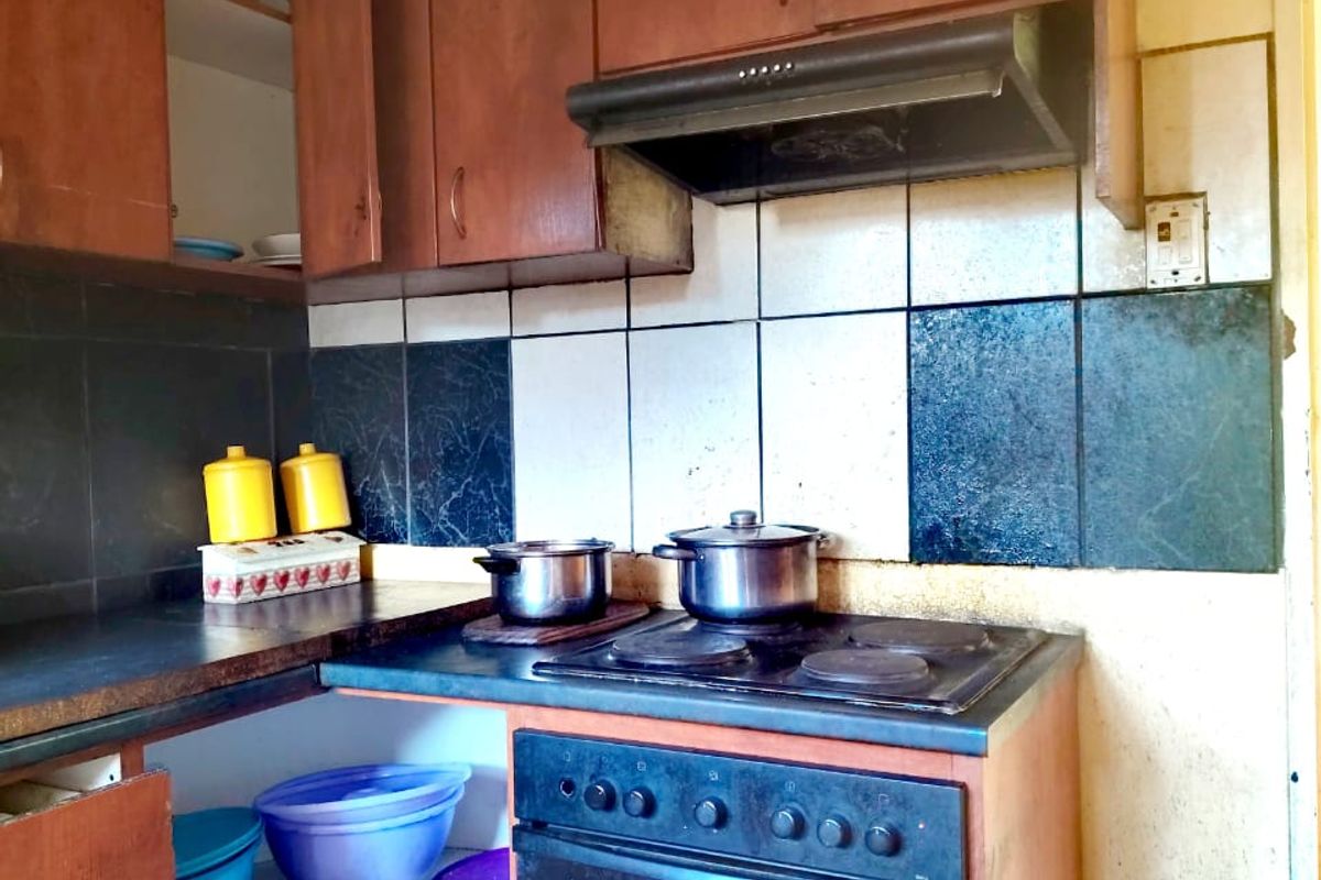 A dated kitchen featuring built-in wooden cabinetry, an electric stove with extractor fan, and a tiled backsplash, requiring cosmetic updates and repairs.