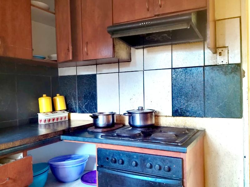 A dated kitchen featuring built-in wooden cabinetry, an electric stove with extractor fan, and a tiled backsplash, requiring cosmetic updates and repairs.