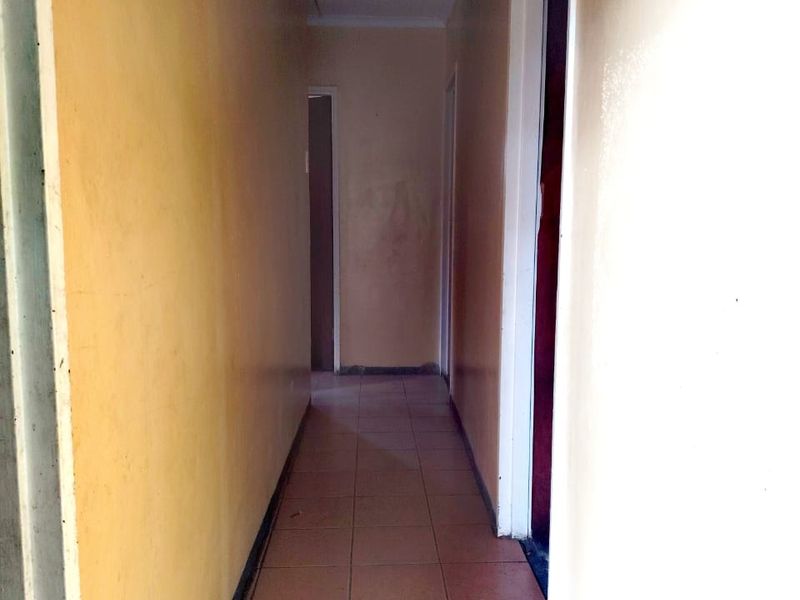 A narrow interior hallway featuring tiled flooring and a damaged ceiling panel with exposed wiring, requiring maintenance and cosmetic updates.
