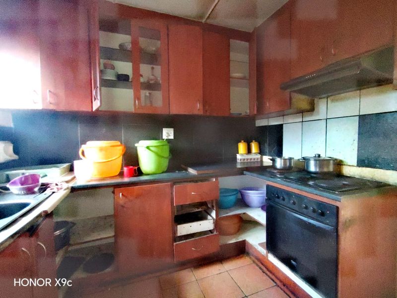 A dated kitchen featuring built-in cabinetry, an integrated oven and hob, and tiled finishes, currently requiring maintenance and cosmetic updates.