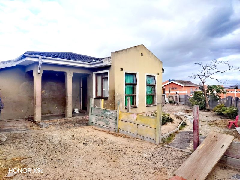Front elevation of a single-story house featuring a covered porch, tiled roof, and a weathered exterior finish with an unpaved front yard.