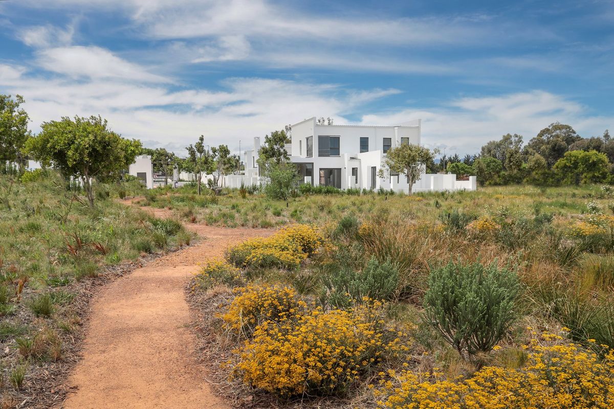 A view of a modern white multi-story residential property set within a natural landscaped environment with a walking path in the foreground.