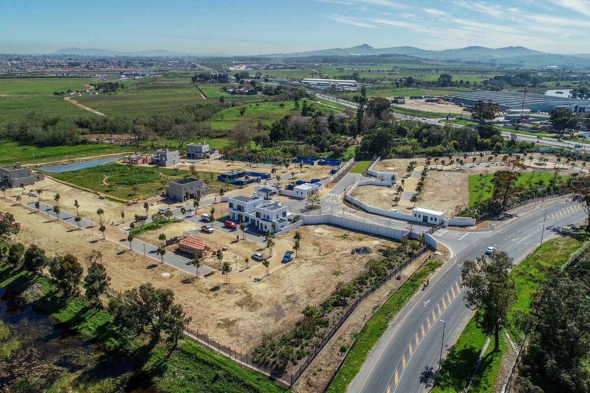 Aerial view of a developing residential estate featuring paved roads, perimeter fencing, and multiple newly constructed modern houses set within a landscaped environment.