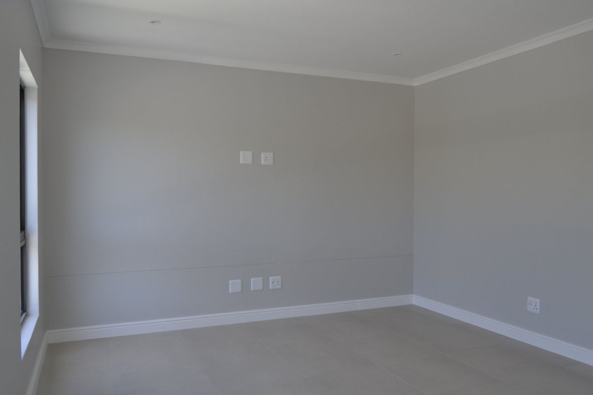 A bright, empty living room featuring neutral grey walls, tiled flooring, recessed ceiling lighting, and integrated electrical and data points.